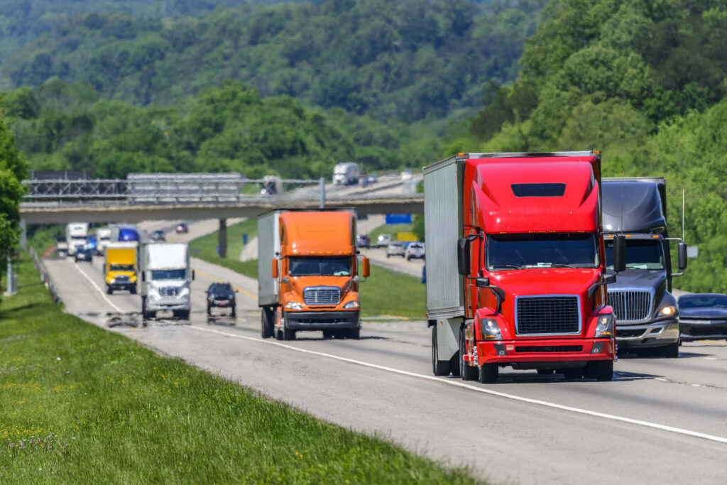 A steady flow of semis lead the way down a busy interstate highway in Tennessee. Heat waves rising from the pavement give a nice shimmering effect to vehicles and forest behind the lead trucks. Excellent reverse copy space across both top and bottom of image.