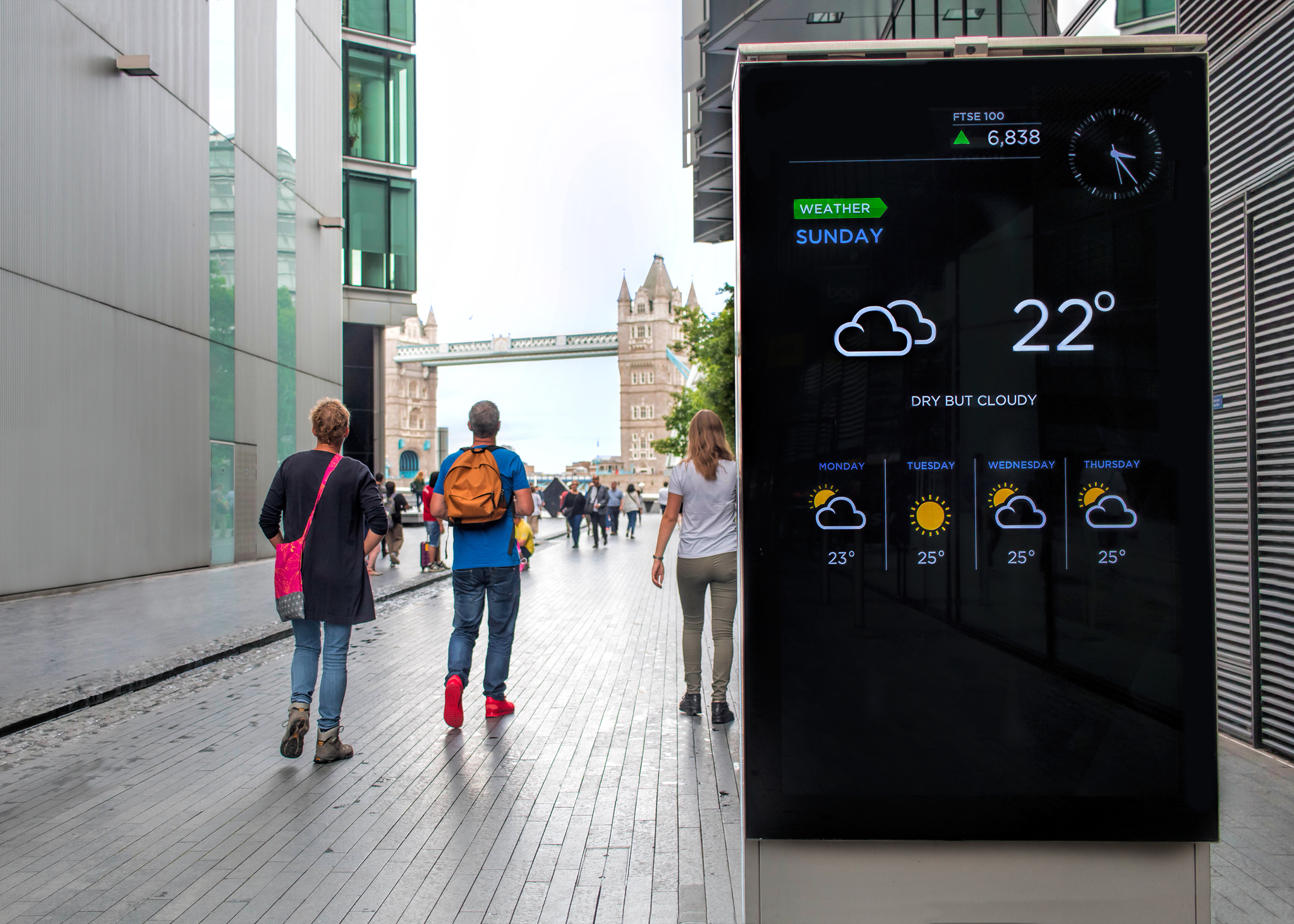 Tourists walking toward Tower Bridge, electronic display with weather forecast.