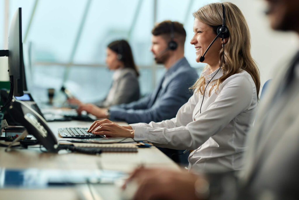 Happy businesswoman and her colleagues working on desktop PC in a call center.