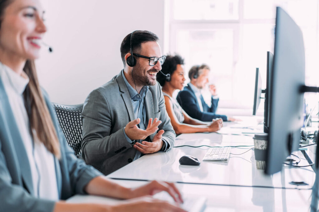 Shot of call center operators working in the office. Call center agent working with his colleagues in modern office. Smiling handsome businessman working in call center.