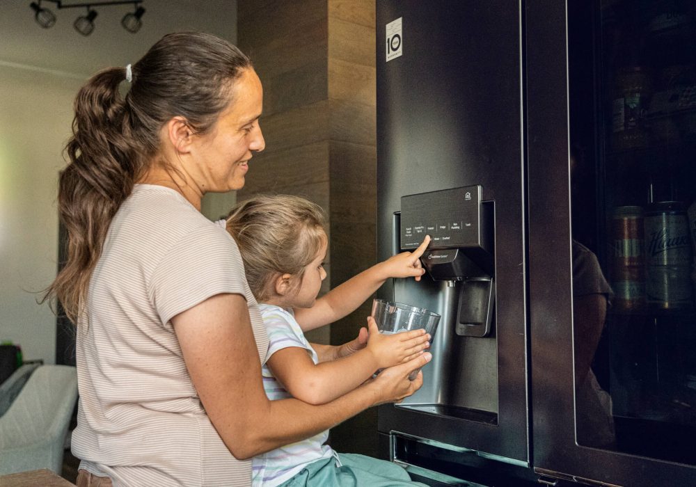 Smart home automations & electricity use in everyday life. Mother & child filling up bowl with ice cubes from ice maker on smart refrigerator for preparation of refreshment drinks.
